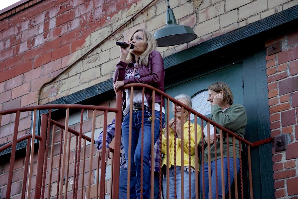 Photo of Shea Amundson of Blue Flame Neon speaks into a microphone while standing at the top of a spiral staircase at the former Poehlmann Hatchery during the neon chick sign lighting ceremony on June 14, 2026. Photo take by Jim Johnson