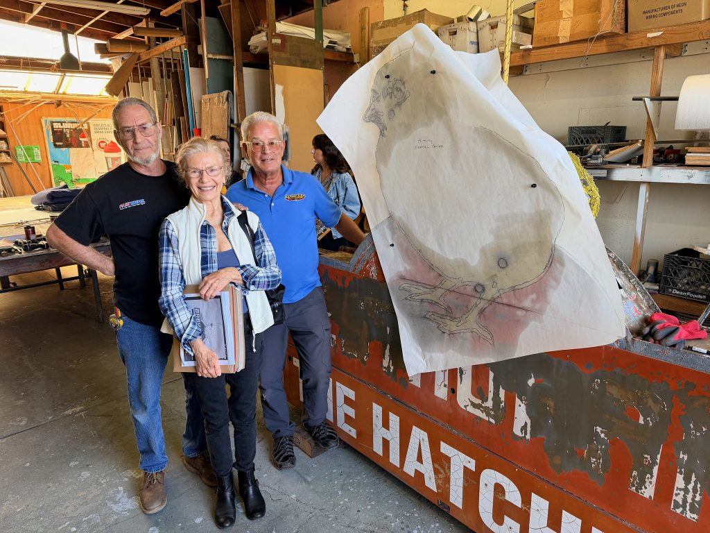 Photo of Mamie Strong, the owner of the neon chick sign, with Mark Barber in black FastSigns t-shirt on the left and Paul Barber in a blue Barber Signs Company t-shirt on the right. Photo taken by Rancall Ann Homan at FastSigns Vallejo shop on April 17, 2026.